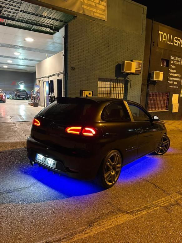 Coche negro con luz azul estacionado afuera de una tienda por la noche.
