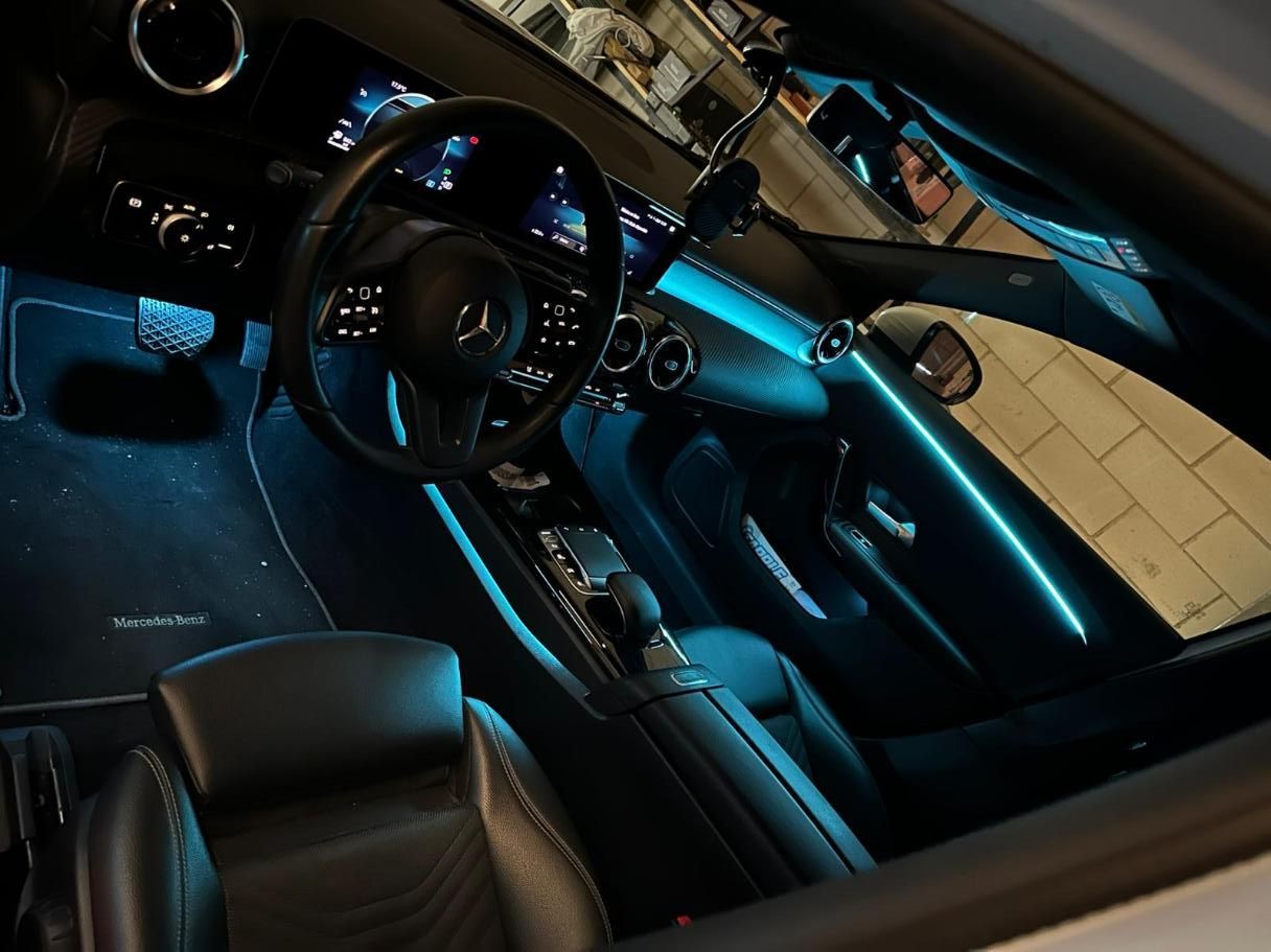 Vista interior de un coche con iluminación ambiental azul. Asientos, volante y salpicadero de cuero negro.