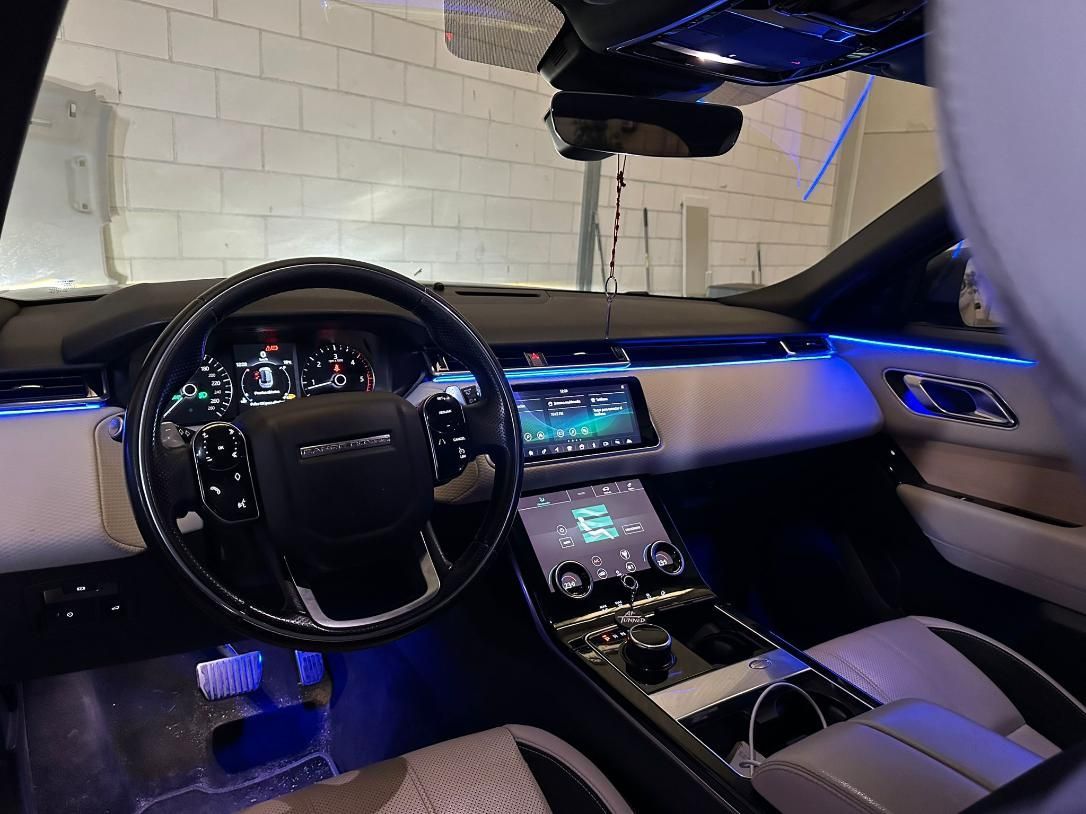 Interior de un Range Rover. Volante negro, salpicadero color crema e iluminación ambiental azul.