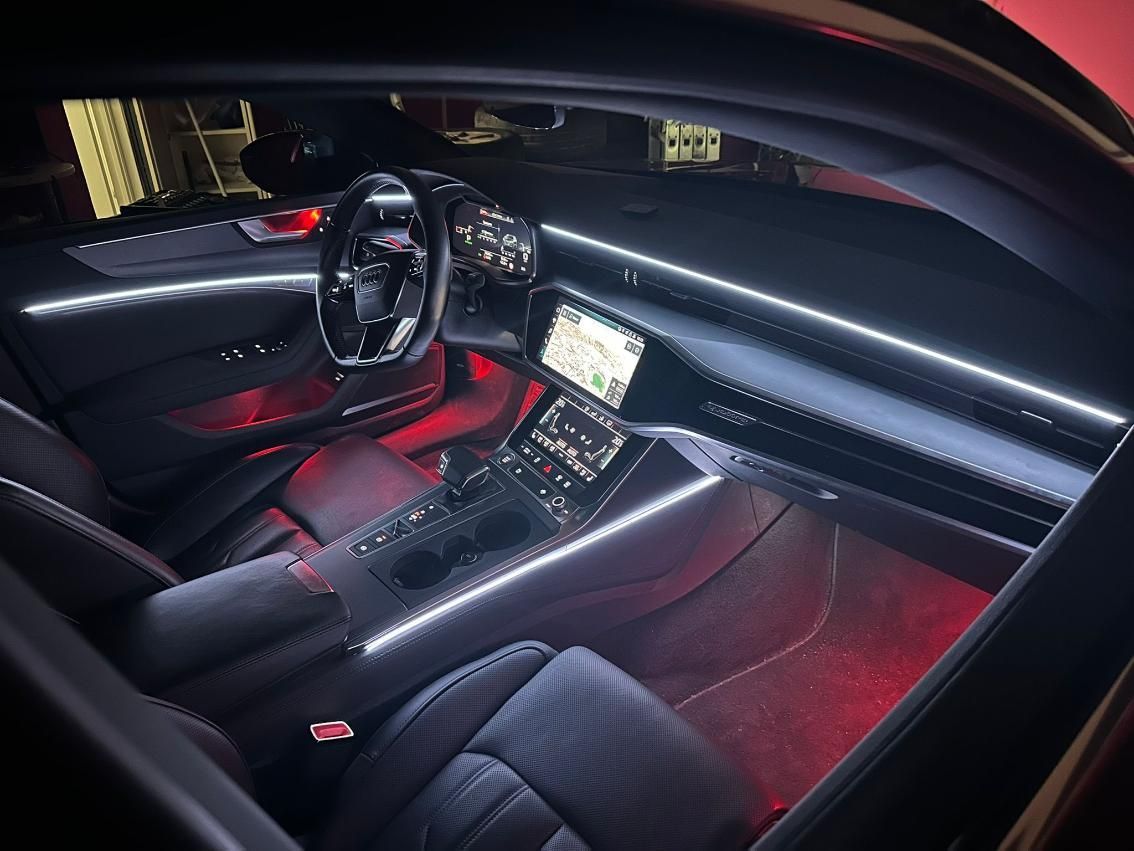 Interior de un coche iluminado con luces LED blancas y rojas. Tablero y consola visibles.