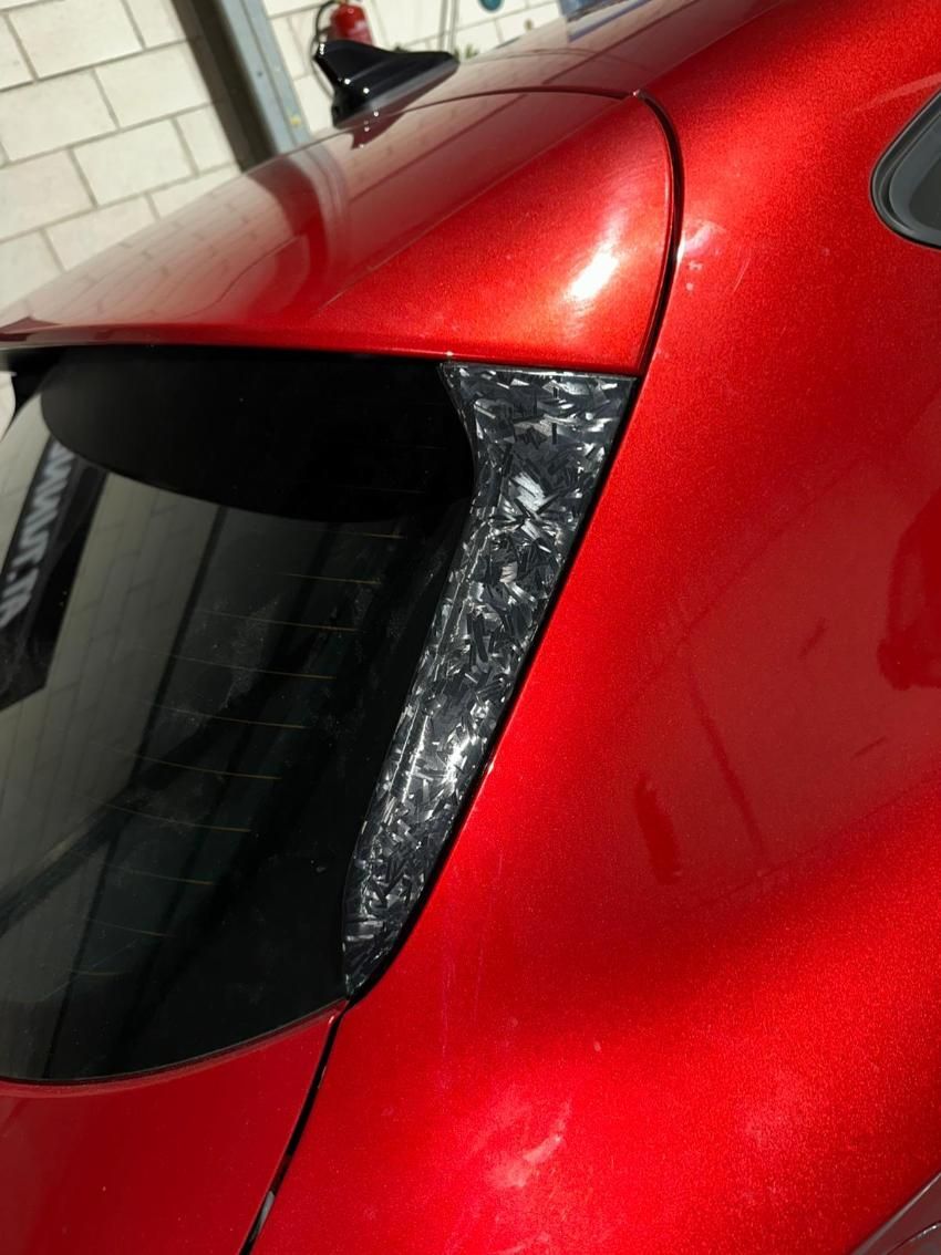 Parte trasera de un coche rojo. Molduras de fibra de carbono alrededor de la ventanilla, con alerón y antena negros.