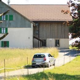 Une voiture est garée devant un grand bâtiment dans un champ herbeux.