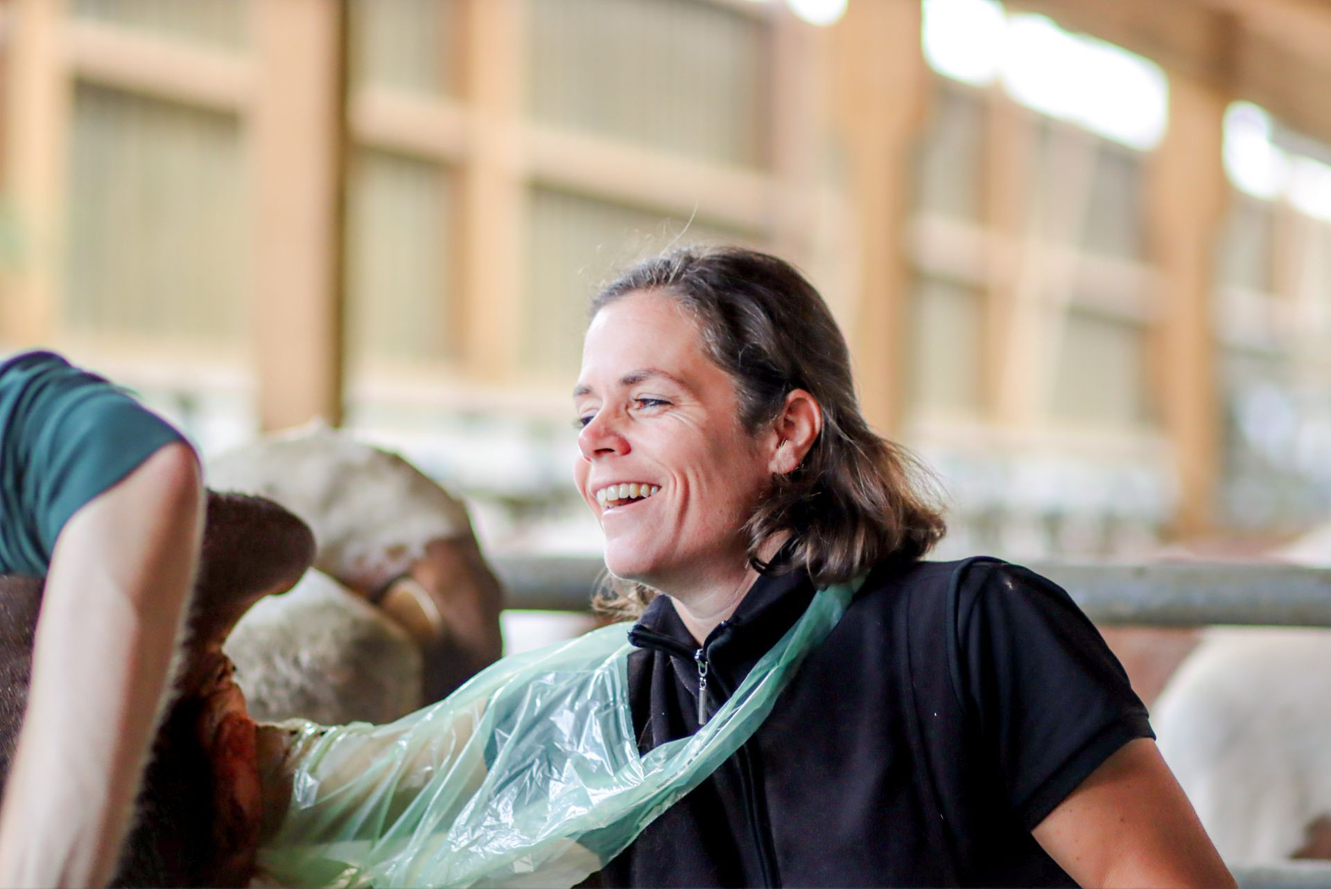 Une femme est assise à côté d'une vache dans une grange et sourit.