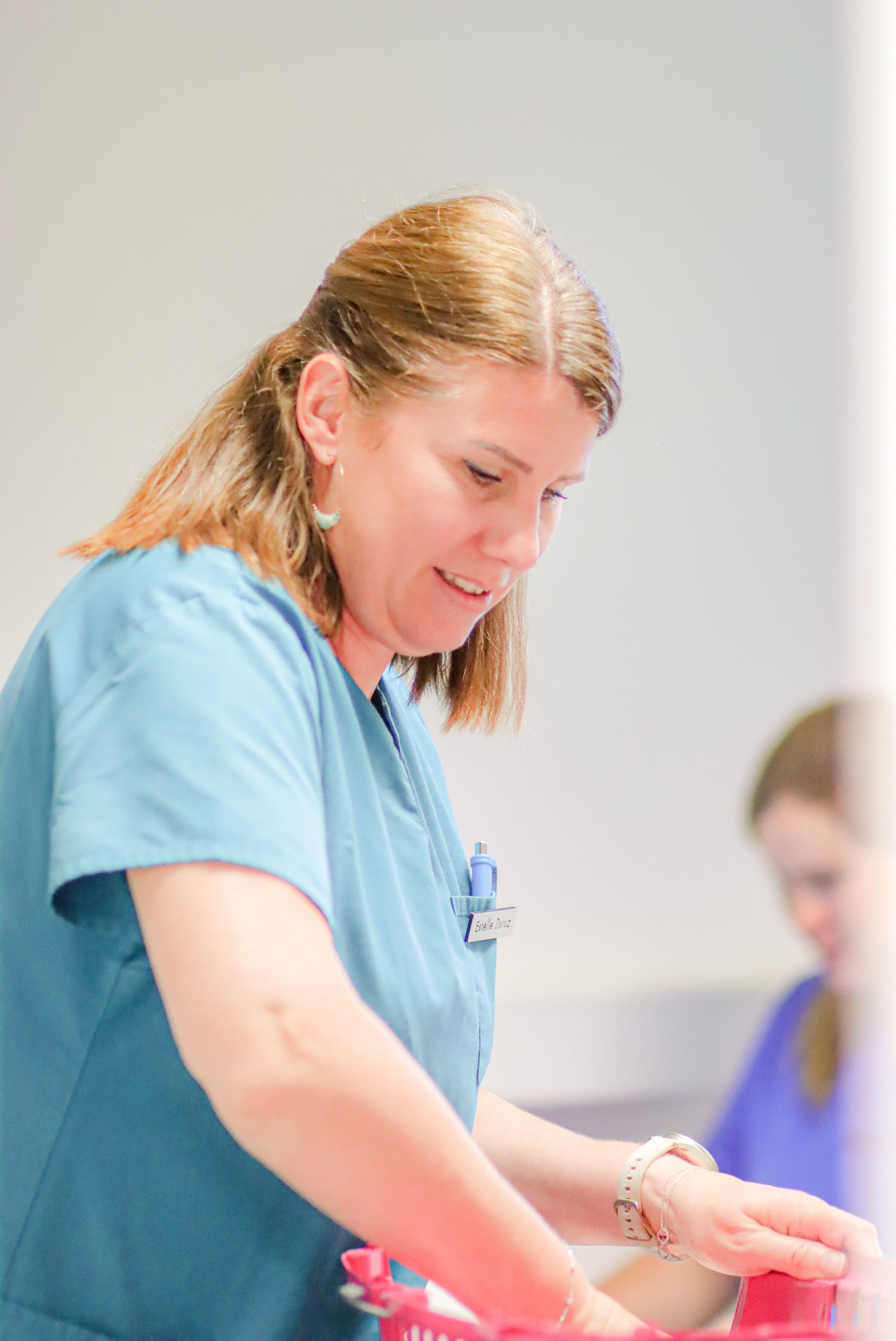Une femme en blouse bleue tient un objet rouge.