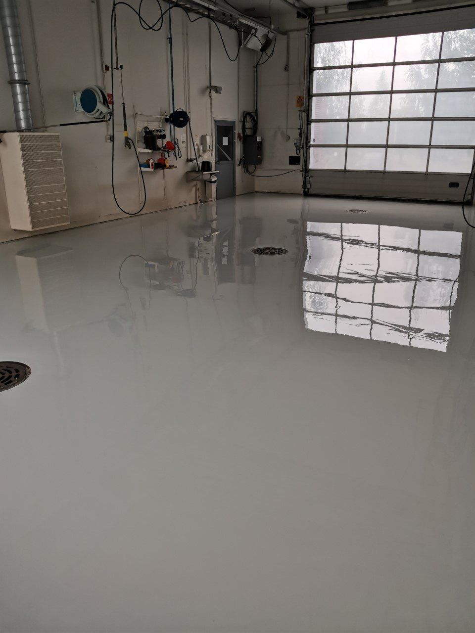 Vaaleanharmaa teollisuuslattia heijastaa autotallin ovea. Muut laitteet on asennettu valkoisille seinille.