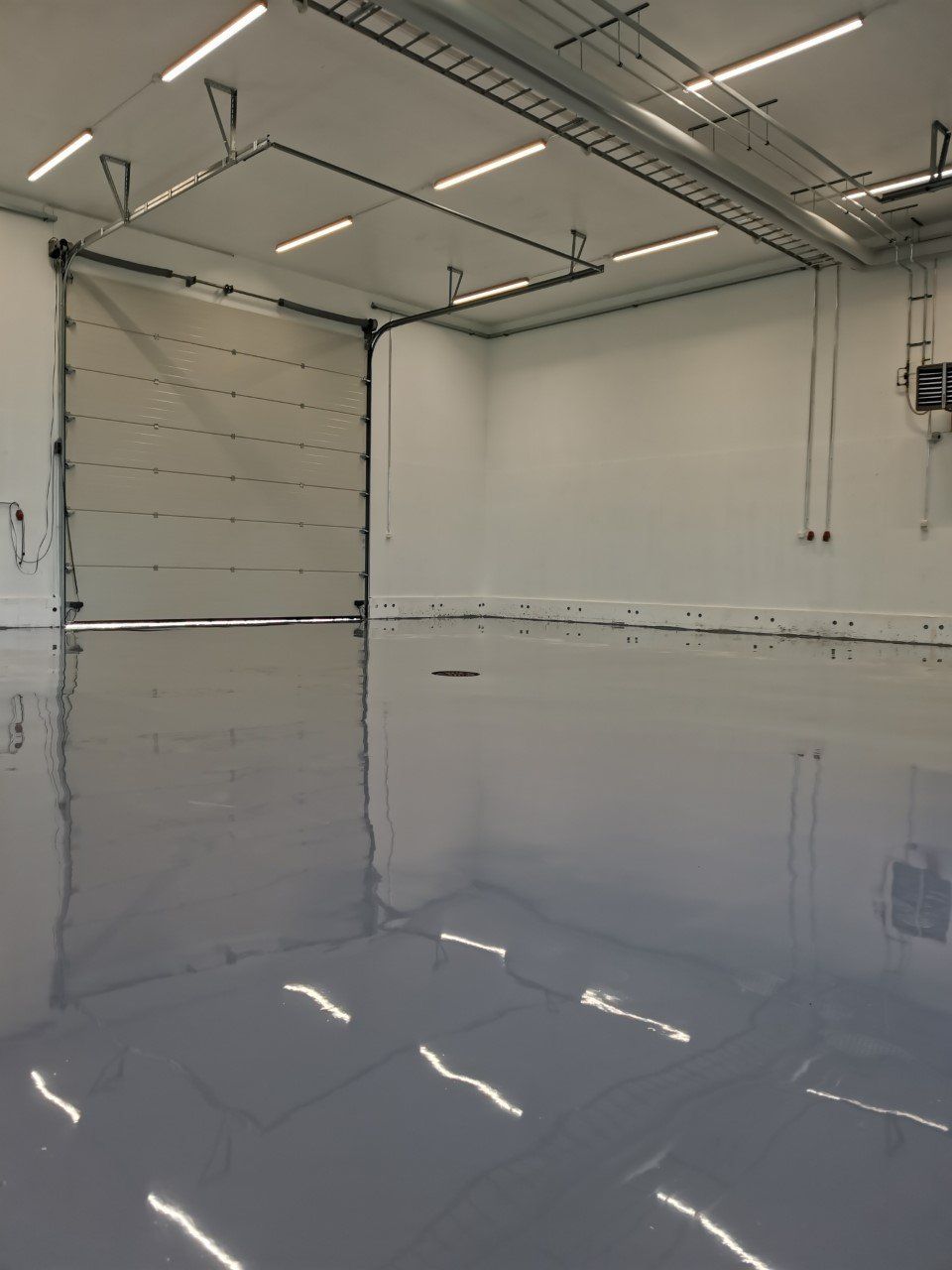 Tyhjä, moderni teollinen varastosisustus, jossa heijastava, harmaa lattia ja suuri suljettu autotallin ovi.