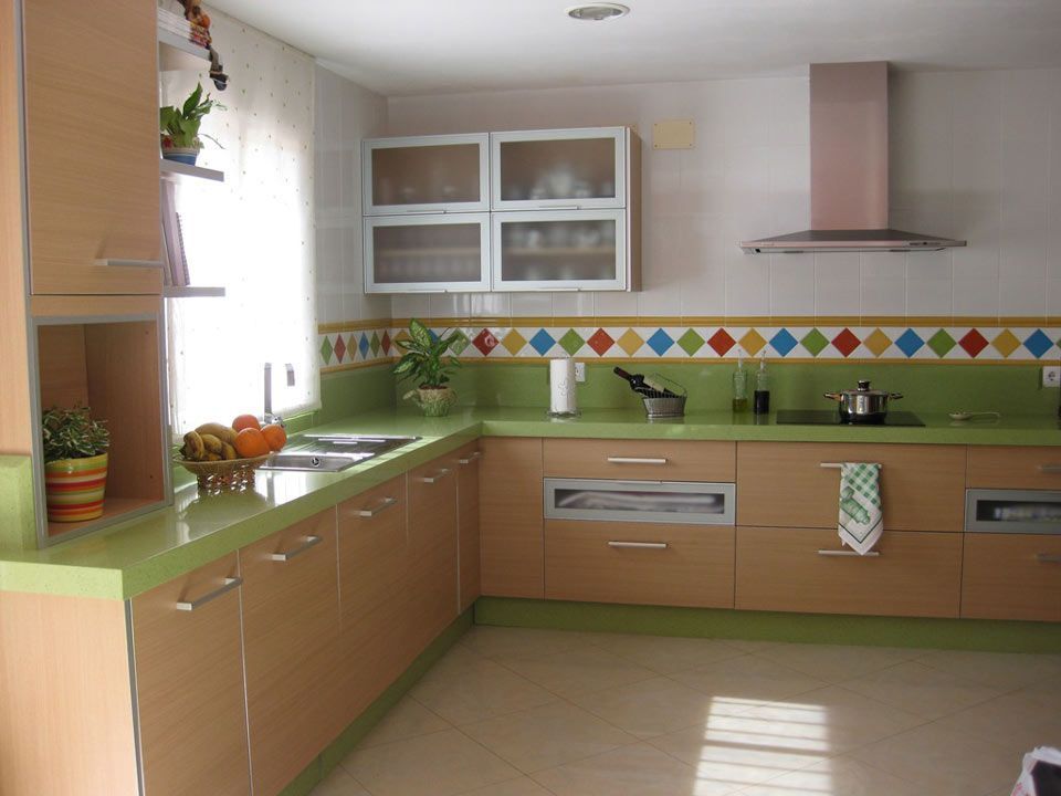 Cocina con gabinetes de madera clara, encimeras y protector contra salpicaduras verdes y azulejos de diamantes de colores.