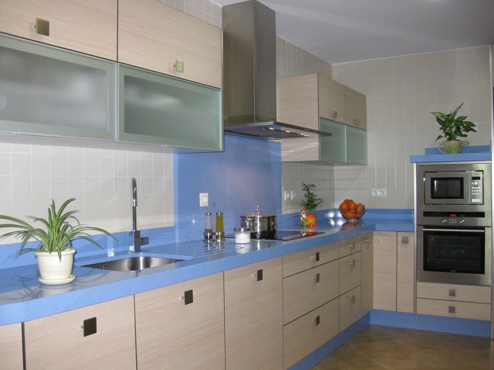 Cocina moderna con gabinetes de madera clara, encimeras azules y electrodomésticos de acero inoxidable.