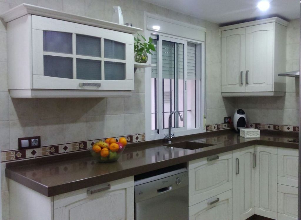 Gabinetes y encimeras de cocina de color crema, un fregadero y una ventana con un frutero.