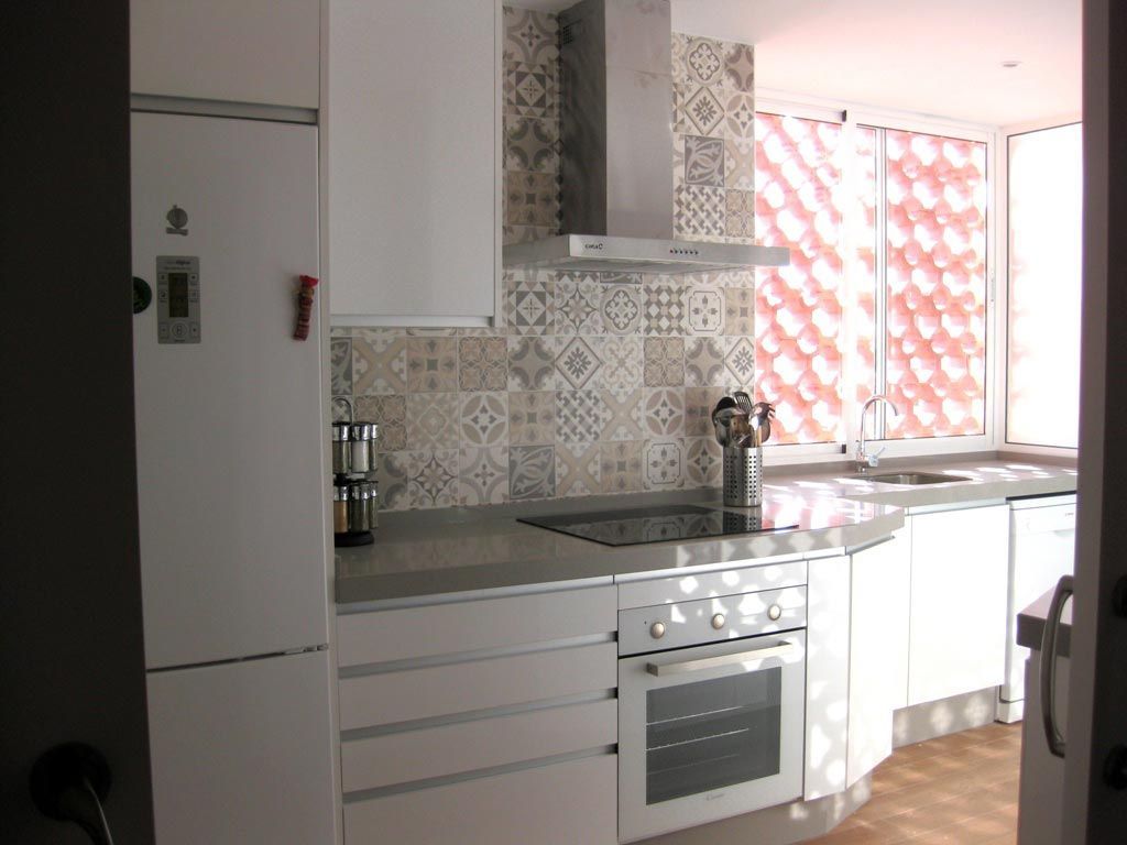 Cocina blanca con encimeras grises, protector contra salpicaduras de azulejos, electrodomésticos de acero inoxidable y una ventana con un patrón rojo.