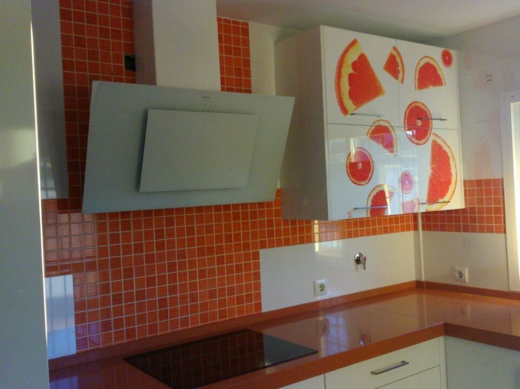 Cocina con salpicadero de azulejos de color naranja, campana de acero inoxidable, armario decorado con frutas y encimera de color naranja.