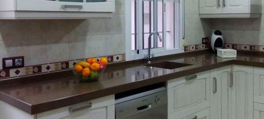 Cocina con gabinetes blancos, encimera marrón y un tazón de fruta.