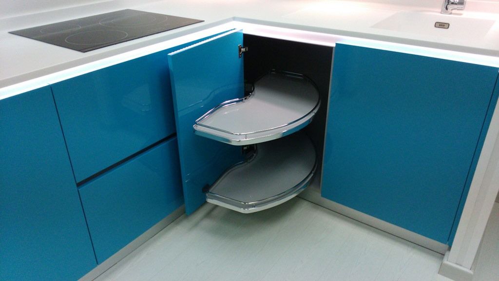 Mueble de cocina esquinero de color azul con estantes extraíbles y giratorios, encimera blanca y placa de cocina negra.