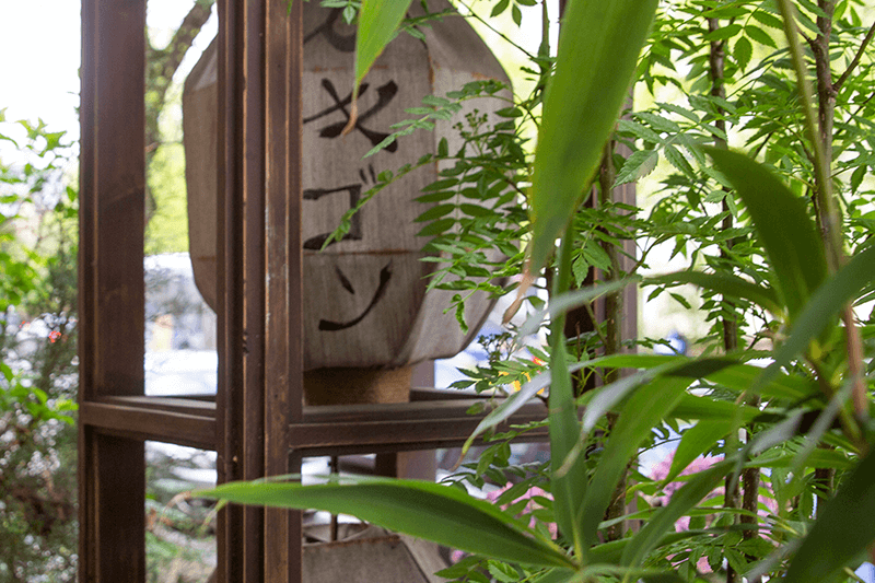 Holzlaterne mit japanischen Schriftzeichen, umrahmt von grünem Laub.
