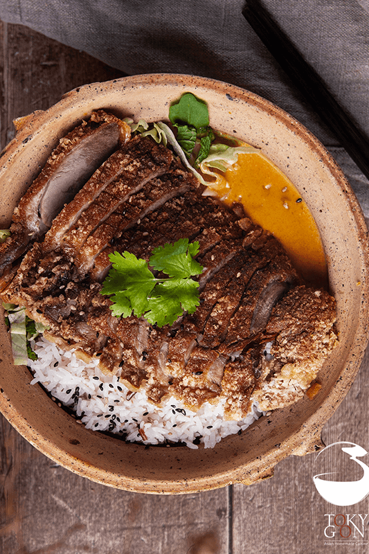 Knusprige Ente mit Reis, Sauce und Gemüse in einer rustikalen Schüssel. Mit Koriander garniert.