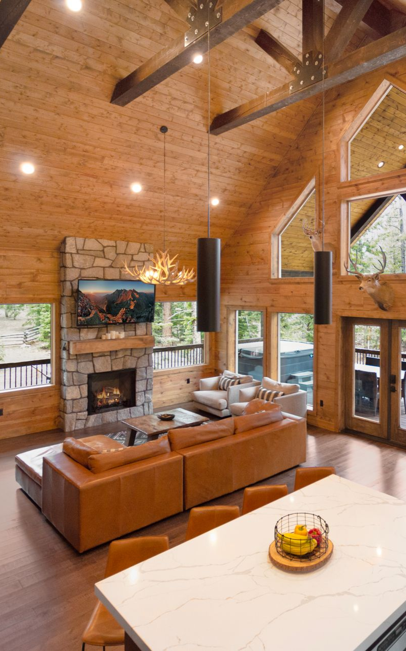 Rustic great room with high ceilings, fireplace, leather sofa, and large windows.