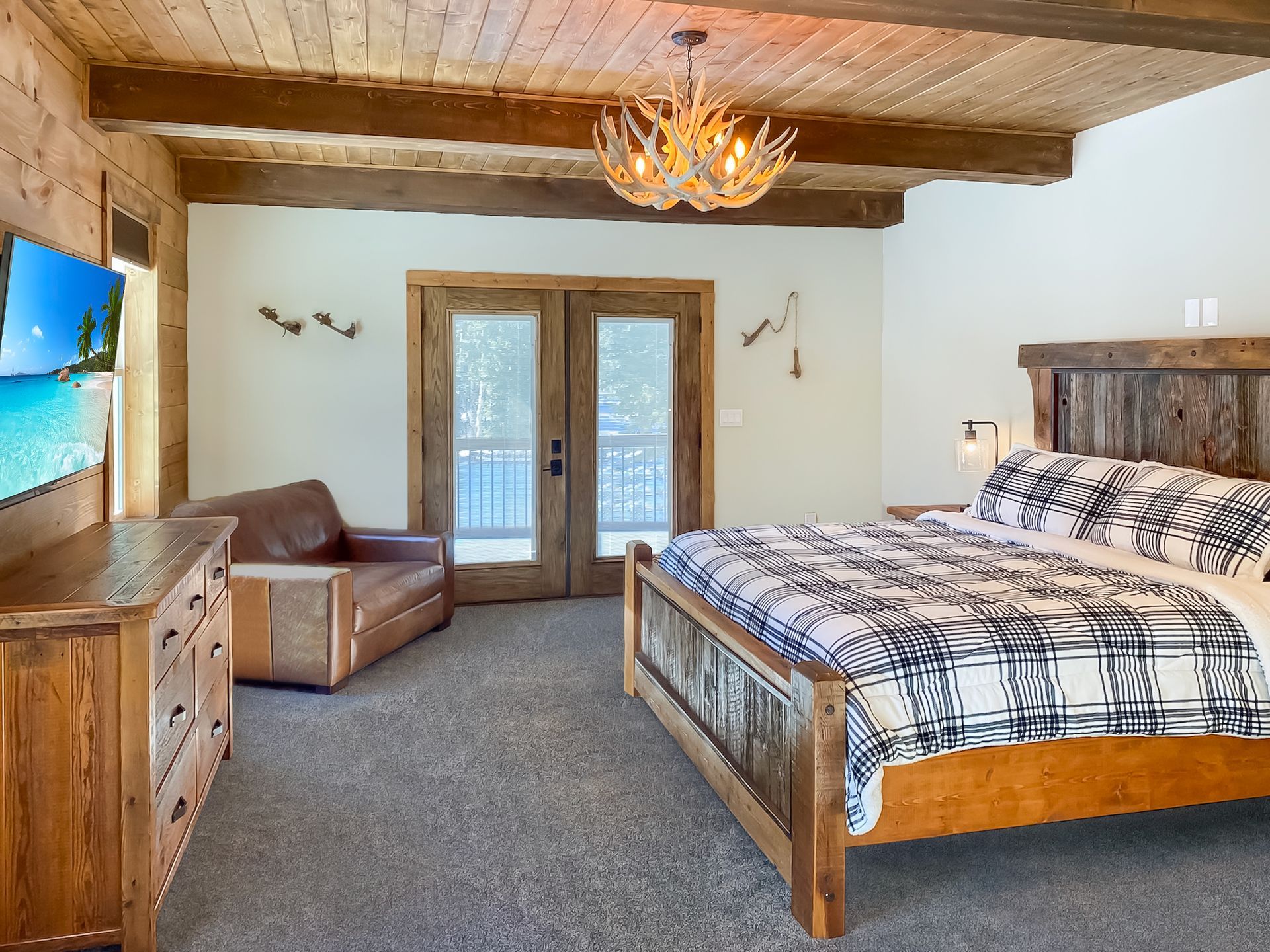 Rustic bedroom with wood beams, a king-sized bed, and a dresser. French doors lead to a balcony.