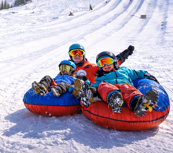 Three people in snow tubes going downhill, smiling with goggles on, on a snowy slope.