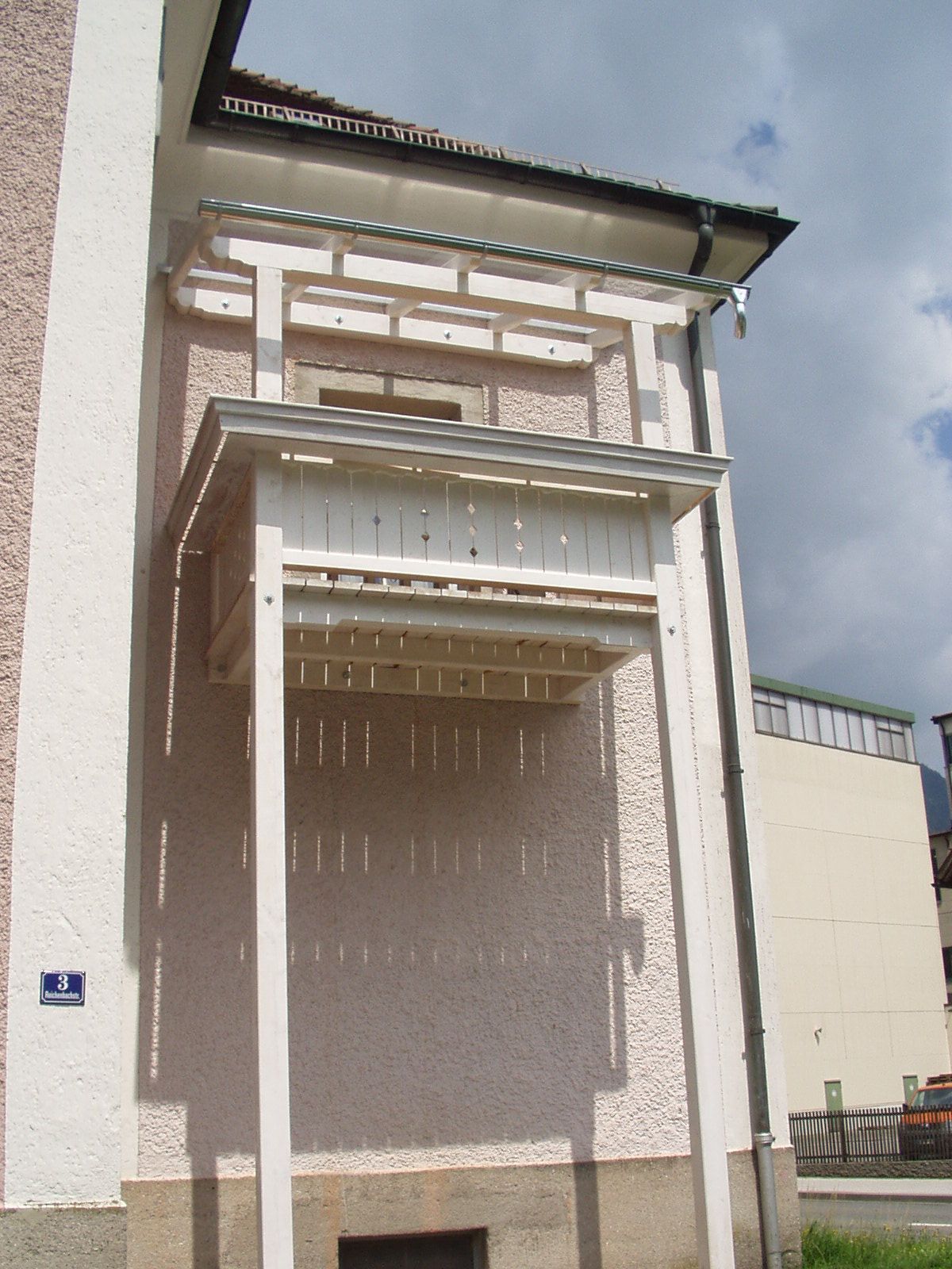 Überdachter Eingangsbereich mit hellen Holzbalken und Balkonaufbau