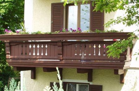 Dunkler Holzbalkon mit verzierten Geländern und Blumenkästen