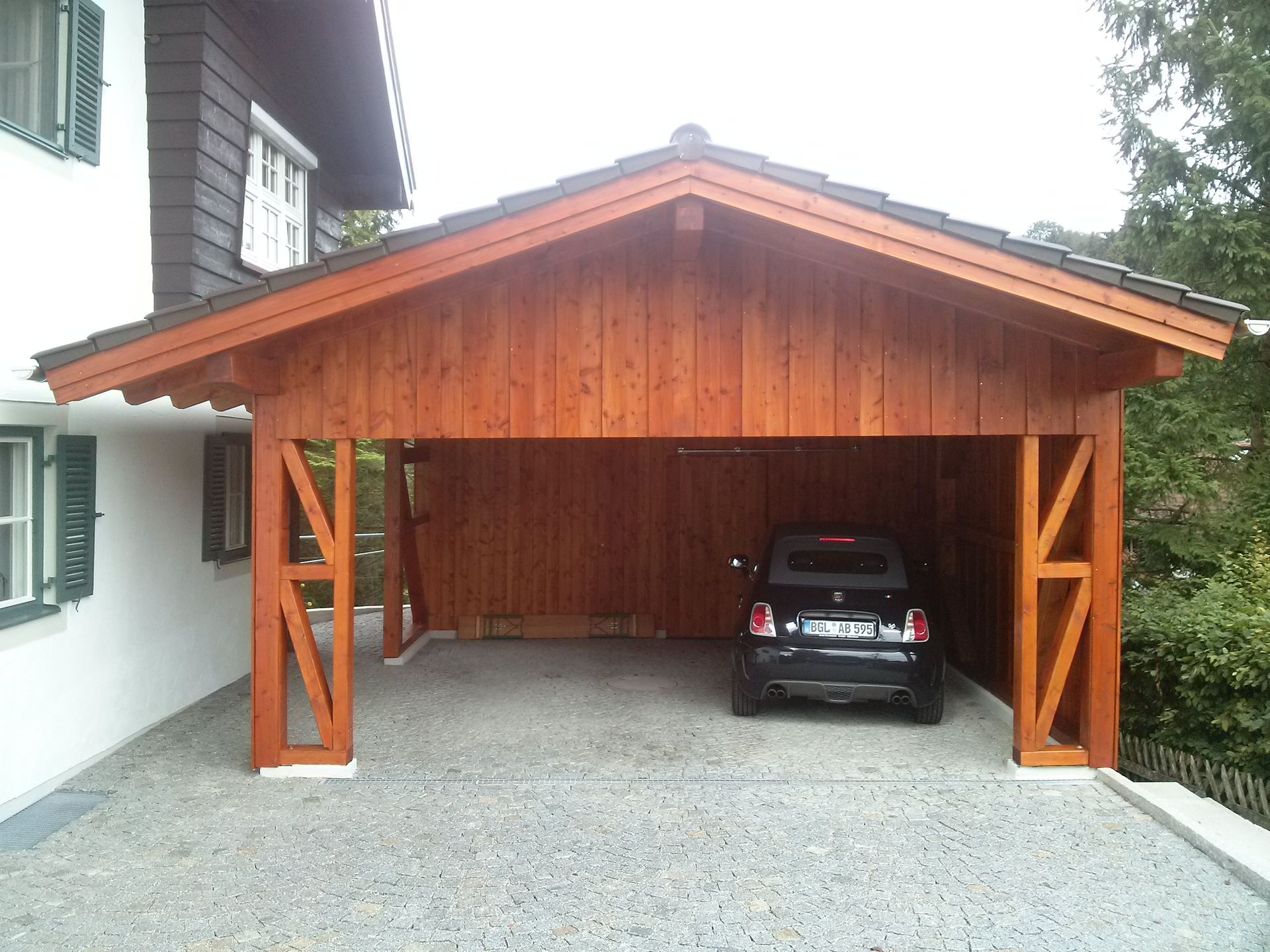 Überdachter Carport aus Holz mit geparktem Auto auf Kiesfläche