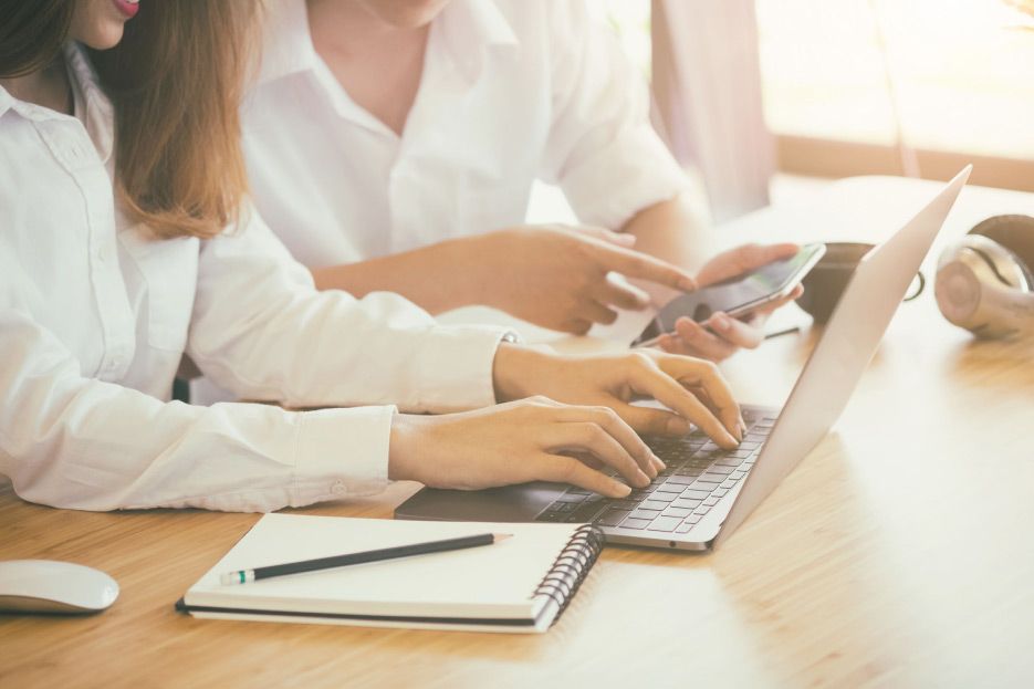 Un hombre y una mujer están sentados en una mesa usando una computadora portátil y un teléfono celular.