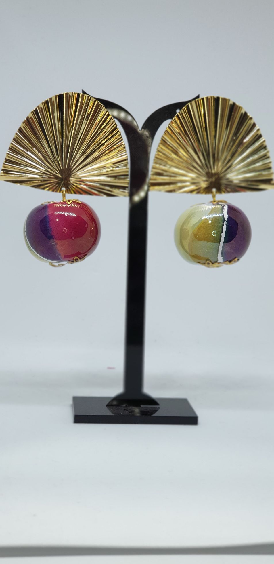 Pendientes de oro con puntas en forma de abanico y colgantes de globos de colores sobre un soporte negro.
