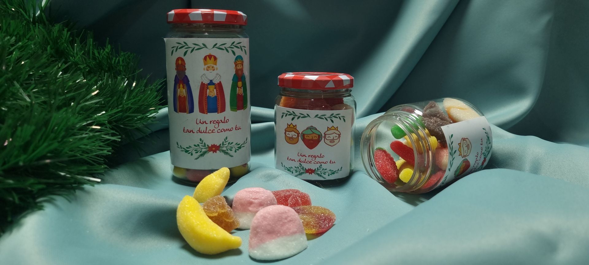 Tarros de caramelos con etiquetas y surtido de gomitas sobre superficie turquesa.