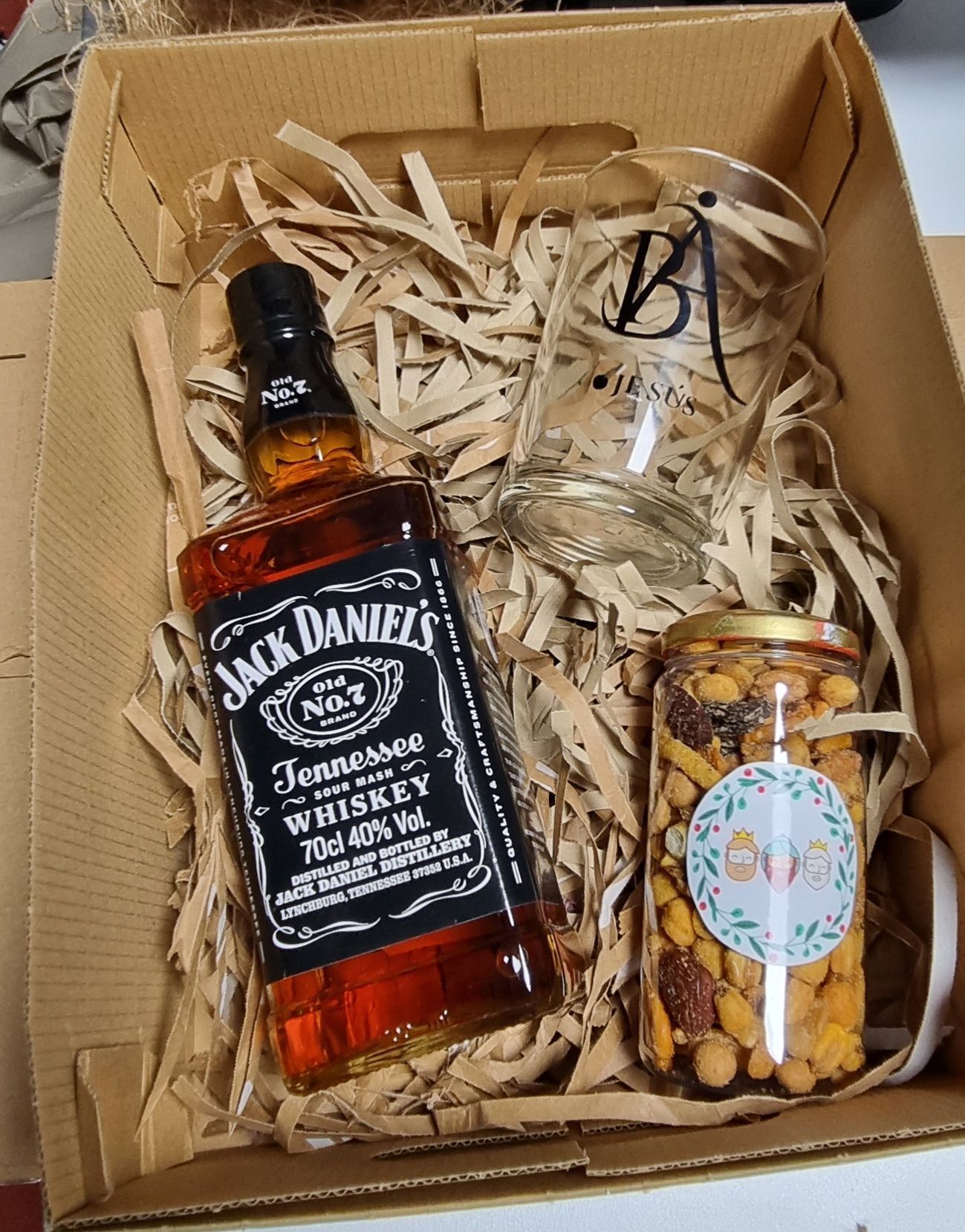 Caja de regalo con whisky Jack Daniel's, un vaso y un tarro de snacks, todo ello envuelto en papel triturado.