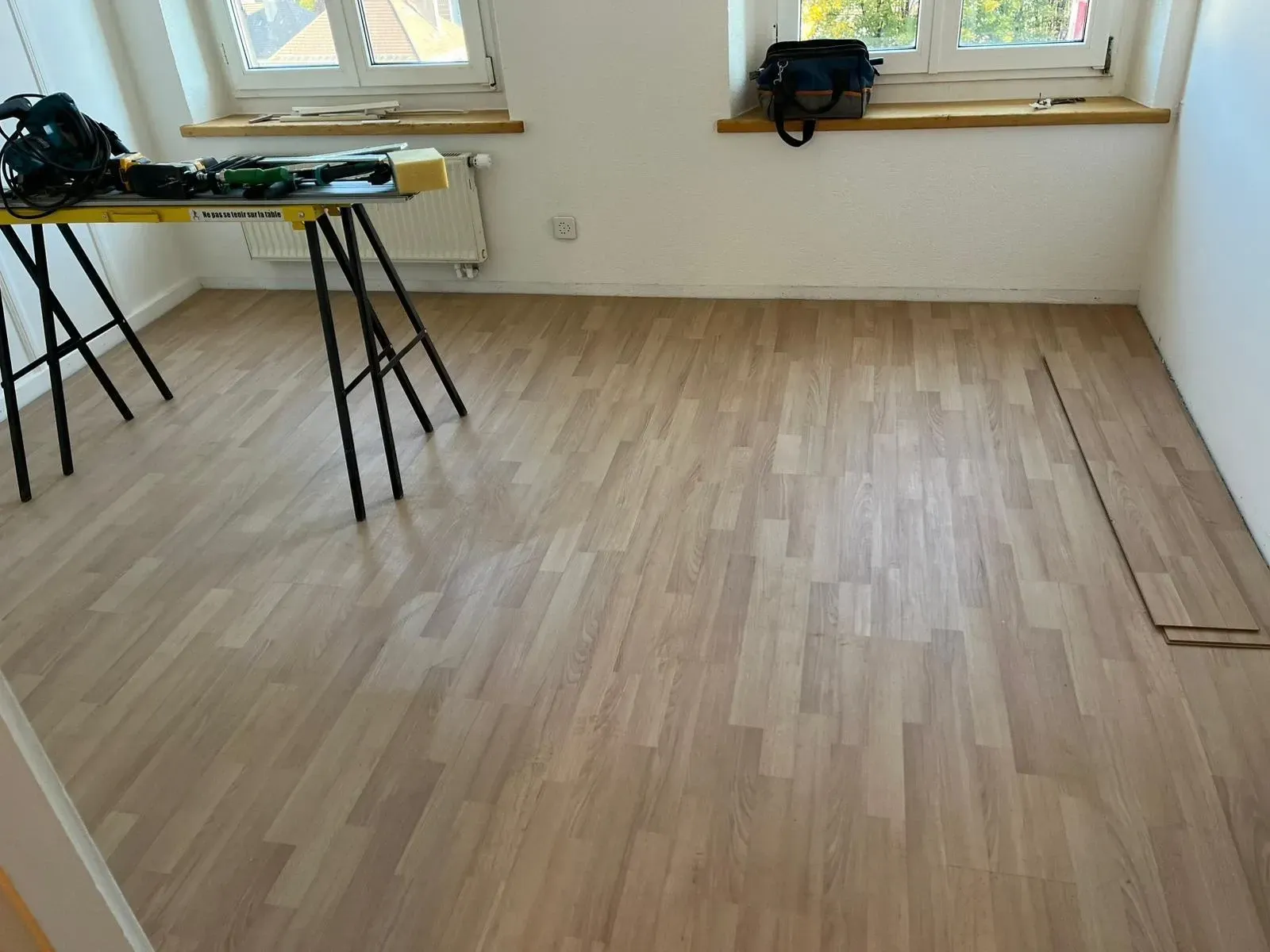 Intérieur vide d'un bâtiment en construction, avec sol en béton, colonnes, poutres apparentes et fenêtres.