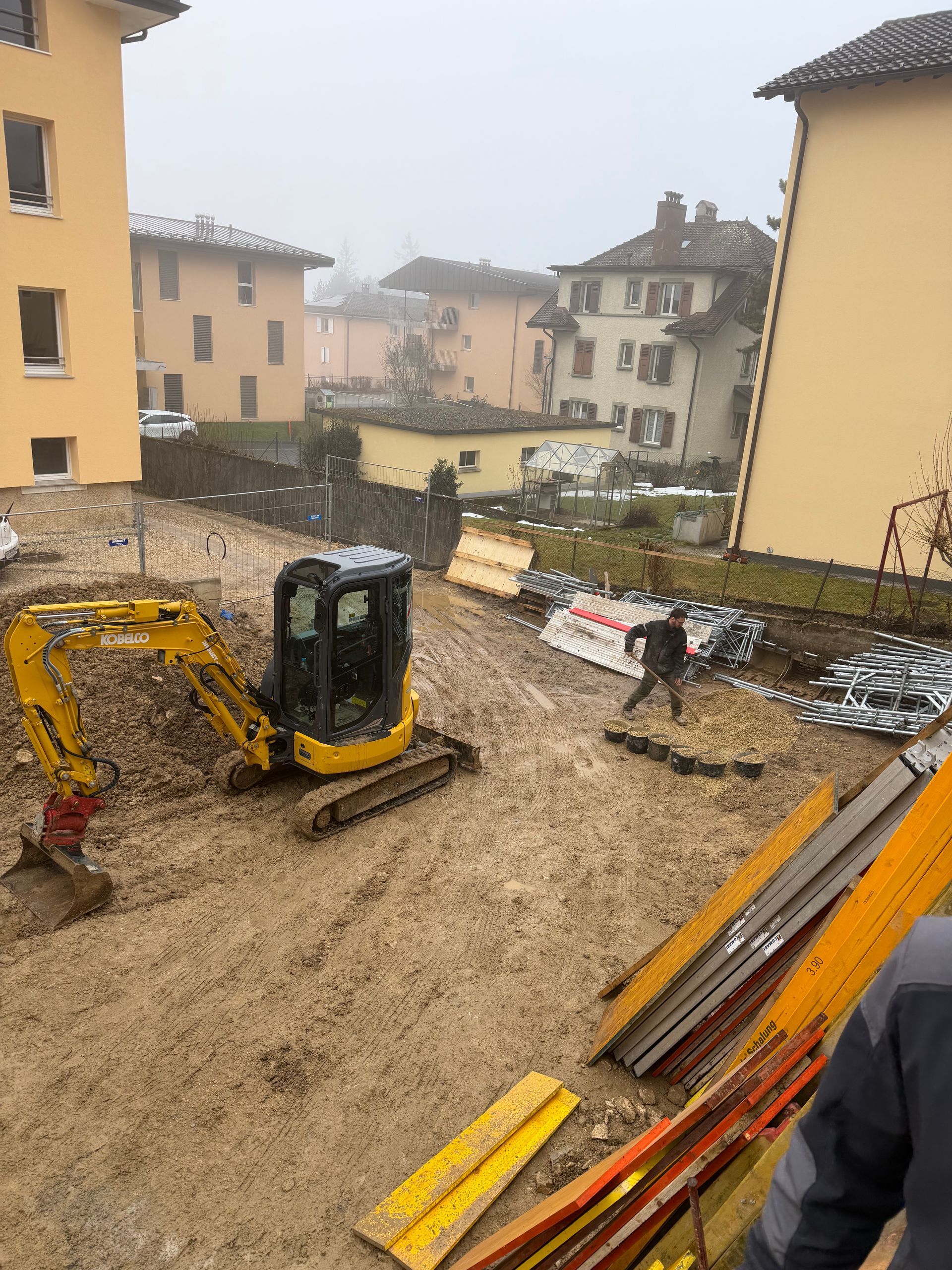 Une excavatrice et une chargeuse compacte se trouvent sur un terrain boueux près d'arbres, probablement un chantier de construction.