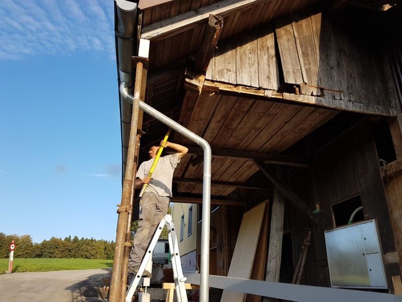 Ein Mann steht auf einer Leiter vor einem Holzgebäude. Foto von der AK Holzwerkstatt GmbH