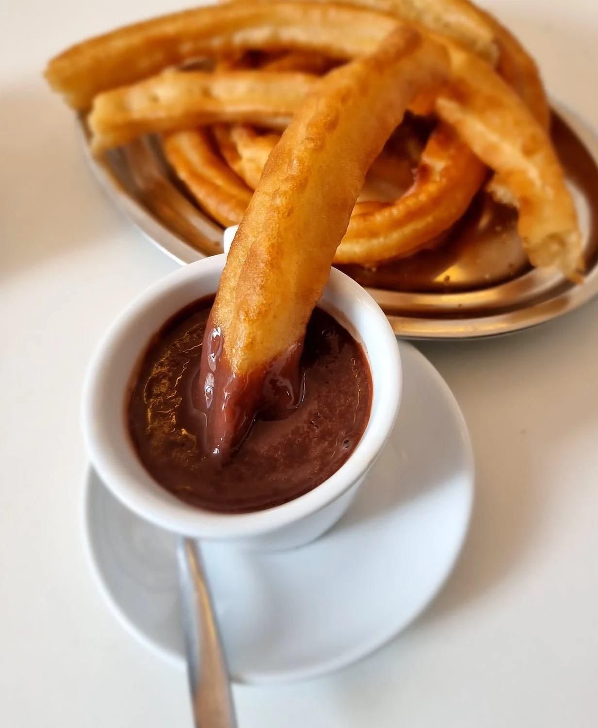 Churro bañado en chocolate intenso, servido con más churros en un plato de plata.