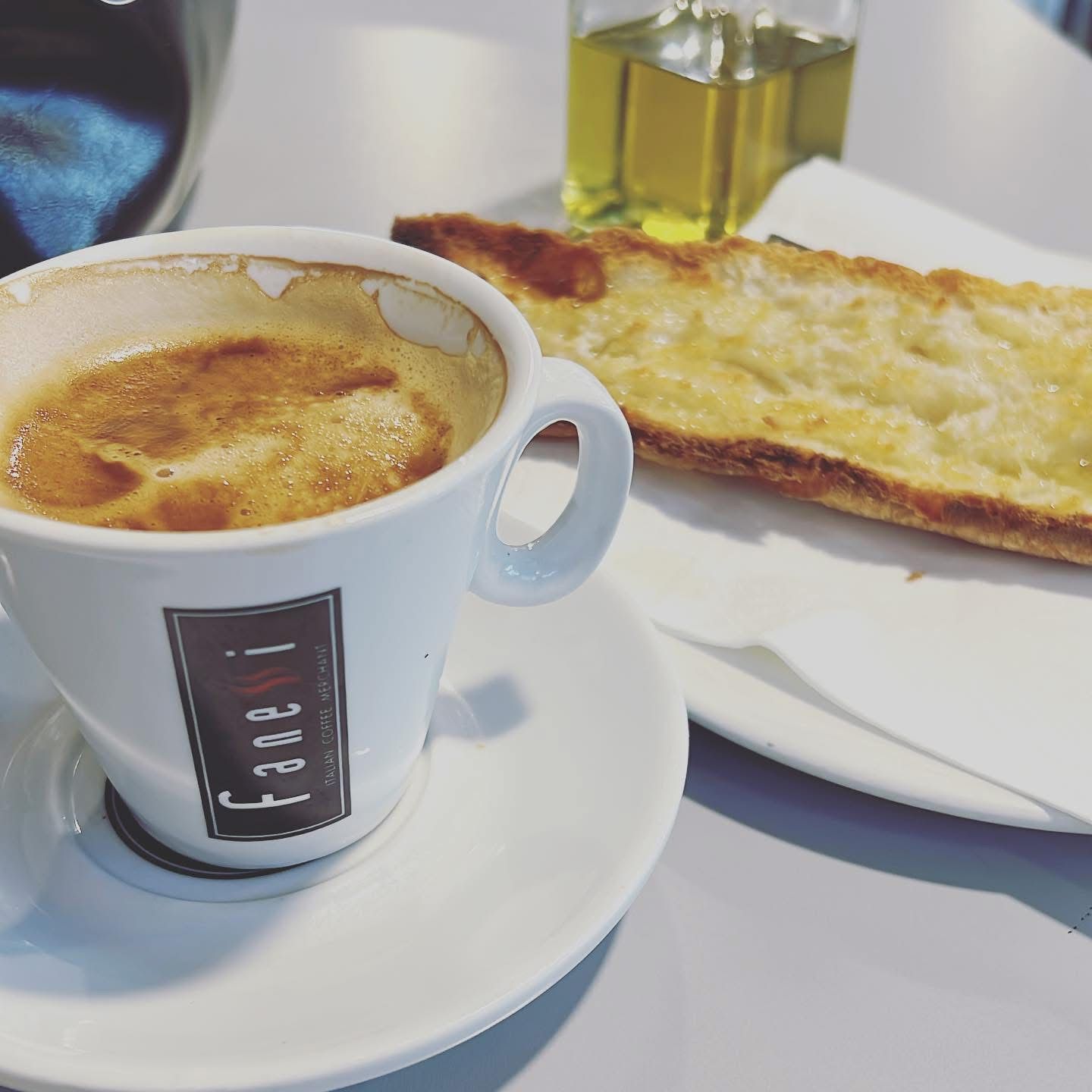 Café en taza blanca, pan tostado y aceite de oliva, en un plato blanco.