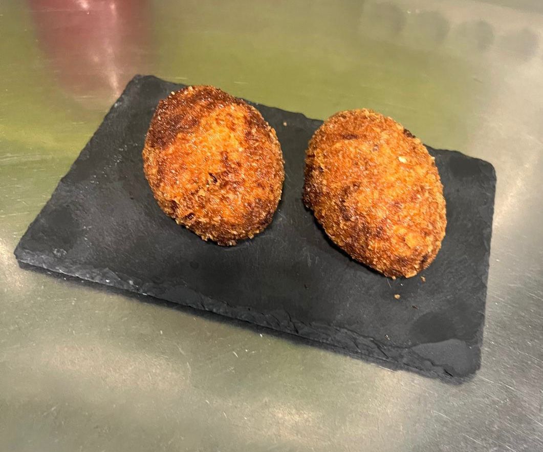 Dos croquetas de color marrón dorado sobre una pizarra rectangular negra.