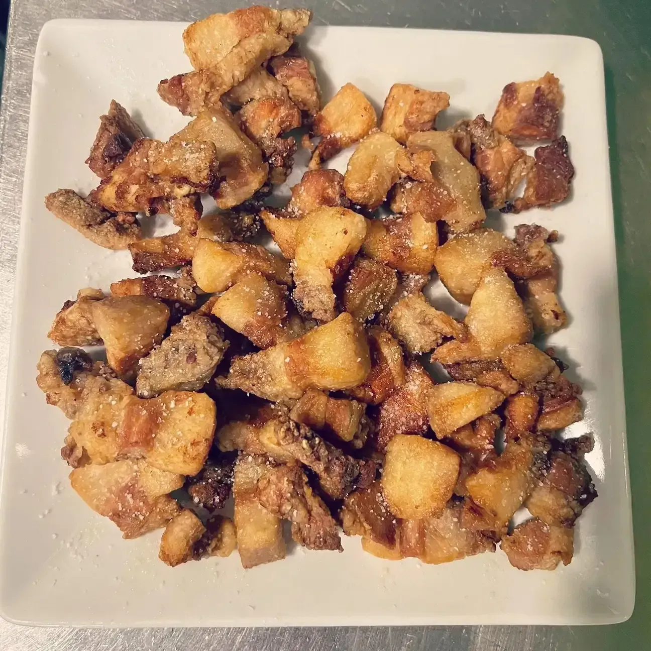 Cubos de panceta de cerdo crujientes, sazonados con sal, sobre un plato cuadrado blanco.