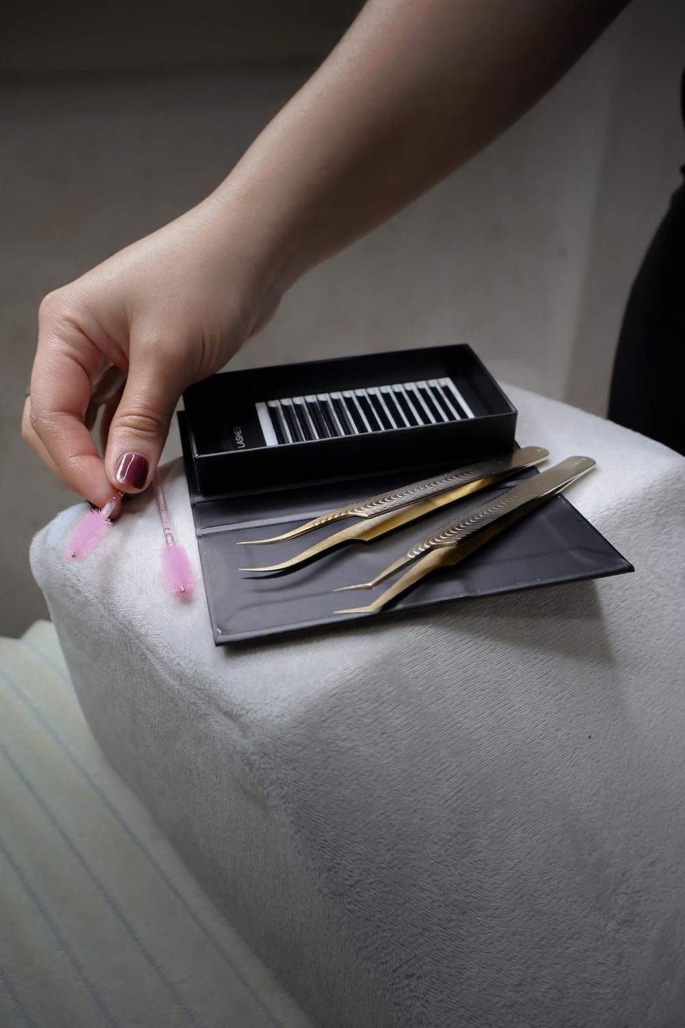 Una mujer sostiene un par de pinzas sobre una caja de extensiones de pestañas.