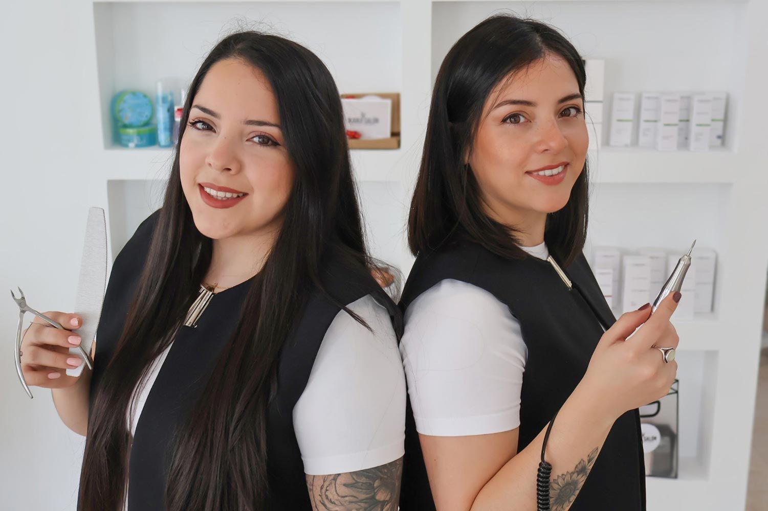 Dos mujeres están paradas espalda con espalda en una habitación sosteniendo tijeras y un teléfono celular.