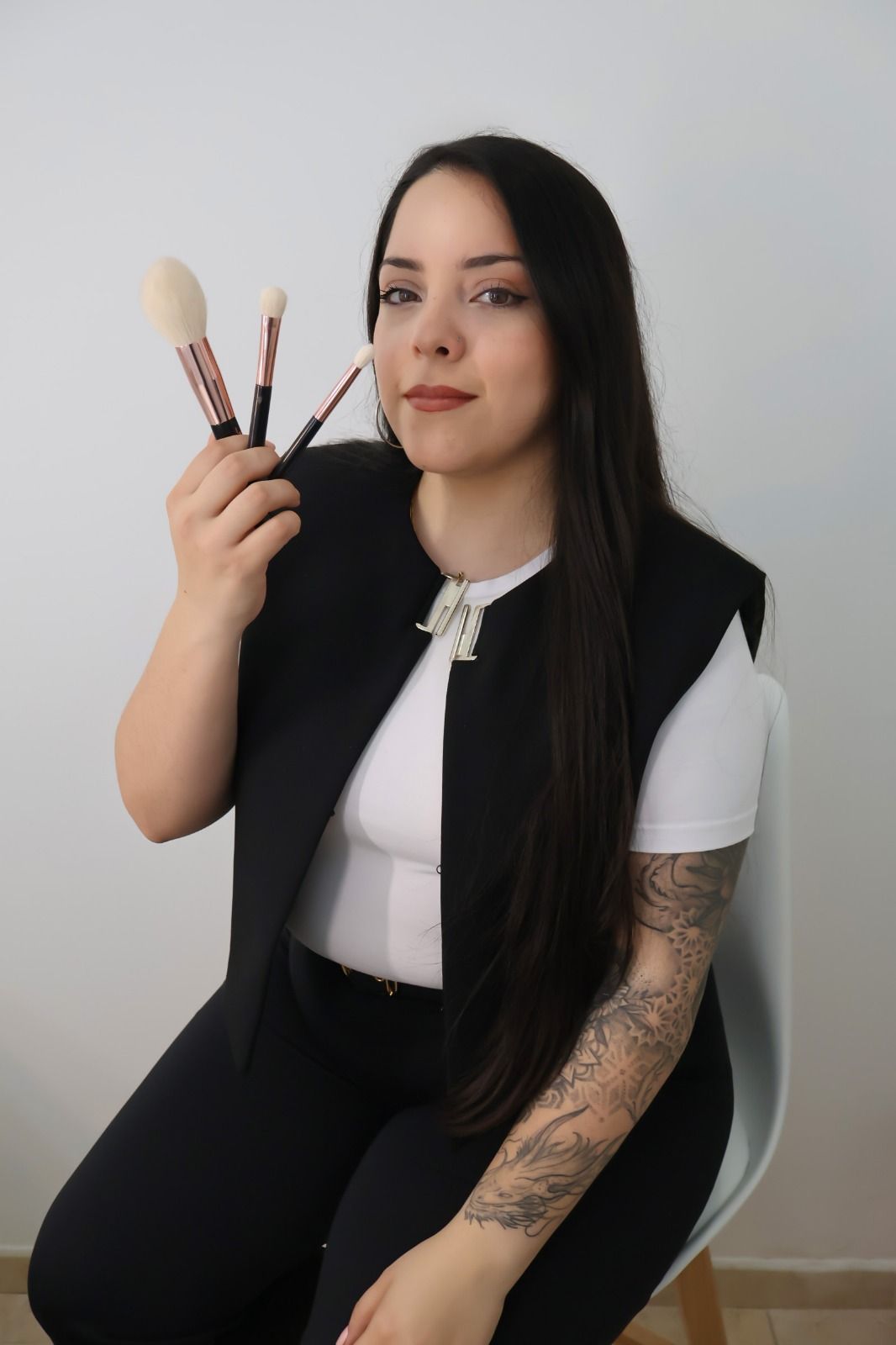 Una mujer está sentada en una silla sosteniendo pinceles de maquillaje.