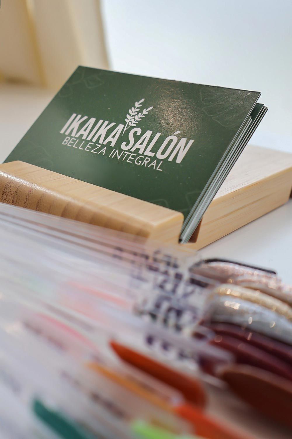 Una tarjeta de presentación para el salón Ikka se encuentra en un soporte de madera.