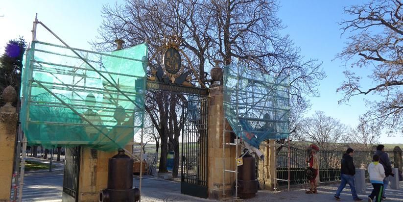 Puerta de entrada con paneles de malla verde y gente caminando a su lado en un día soleado.