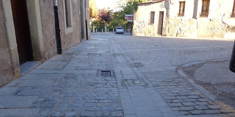 Un estrecho callejón empedrado entre edificios antiguos a plena luz del día, con una pequeña calle enfrente.