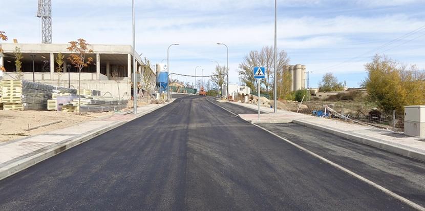Calle pavimentada vacía en una zona escasamente construida, con aceras y postes de servicios públicos bajo un cielo despejado.