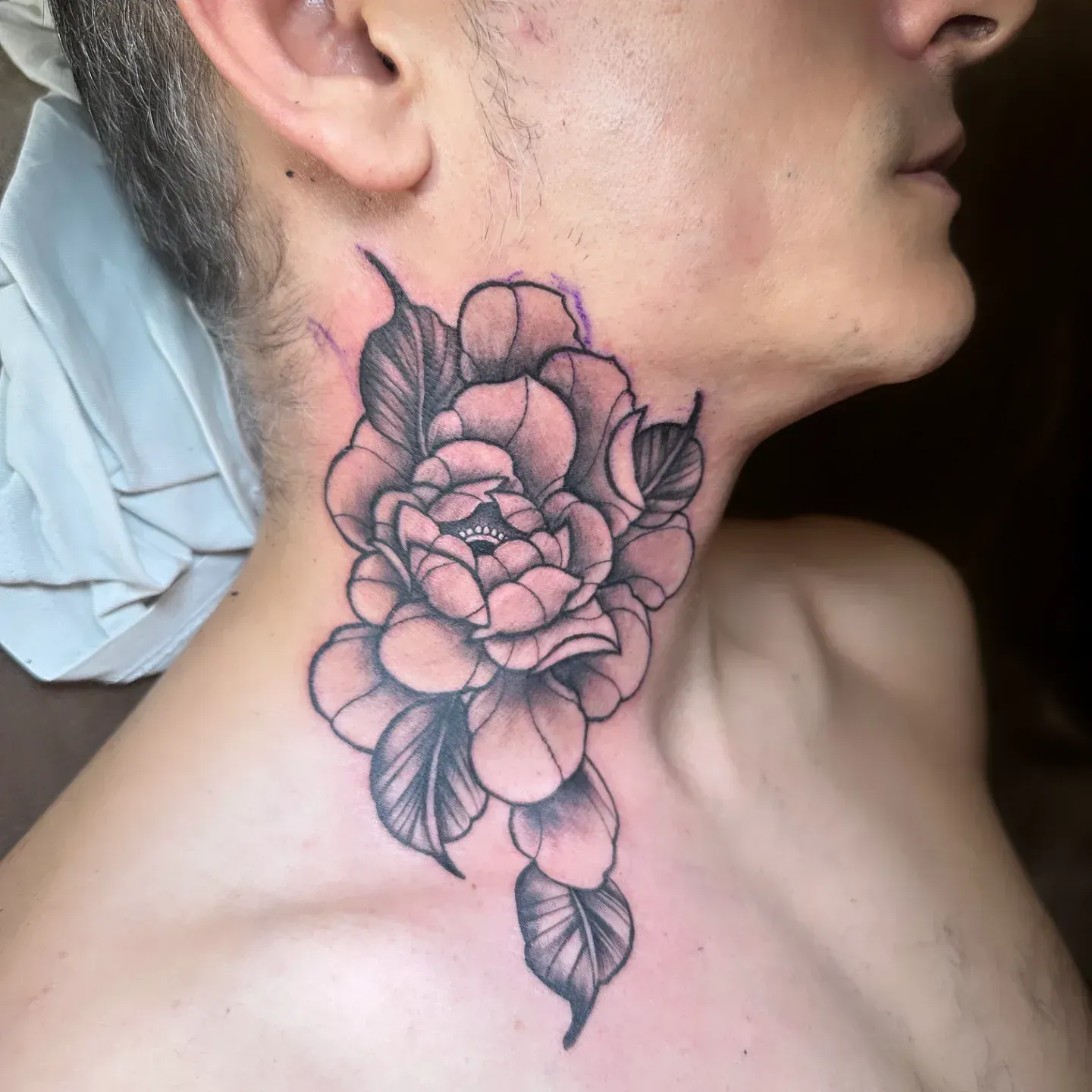 Un hombre tiene un tatuaje de una flor en el cuello.