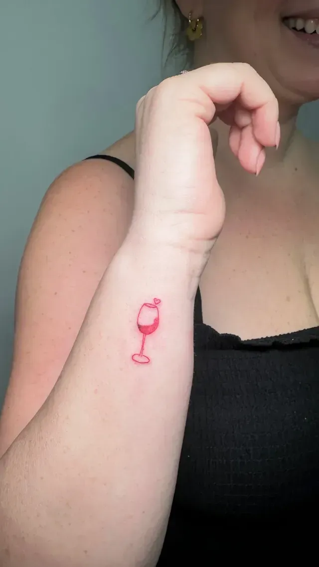 Una mujer tiene un pequeño tatuaje de una copa de vino tinto en su muñeca.