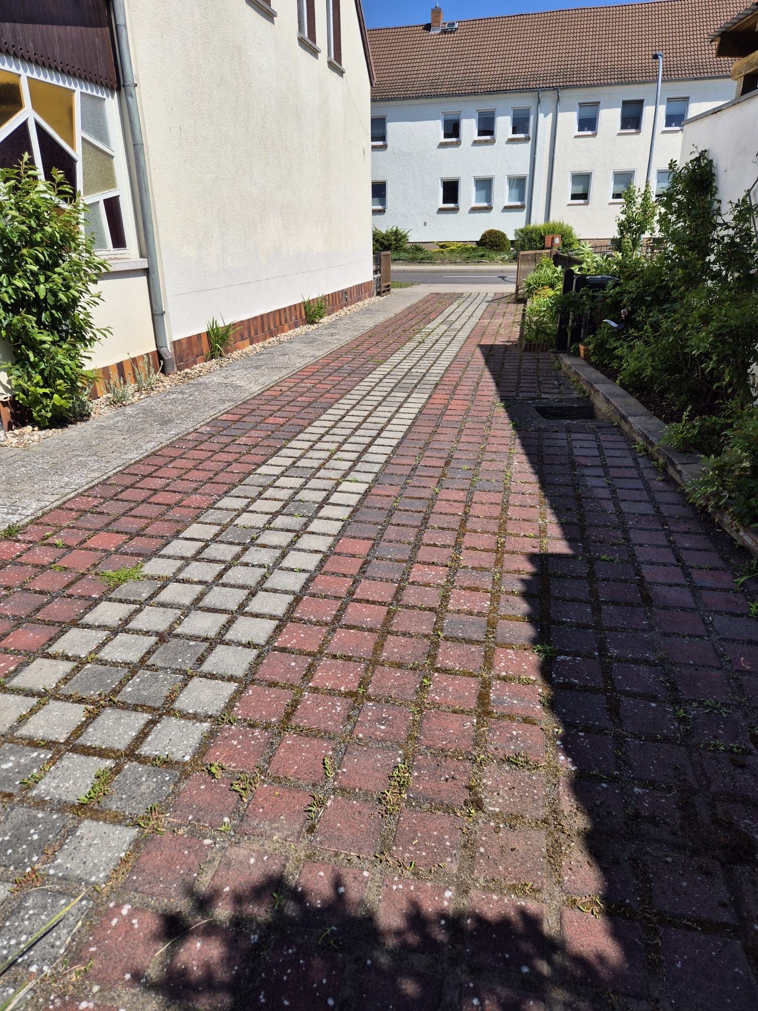 Ein gemauerter Gehweg führt zu einem Gebäude mit einem weißen Gebäude im Hintergrund.