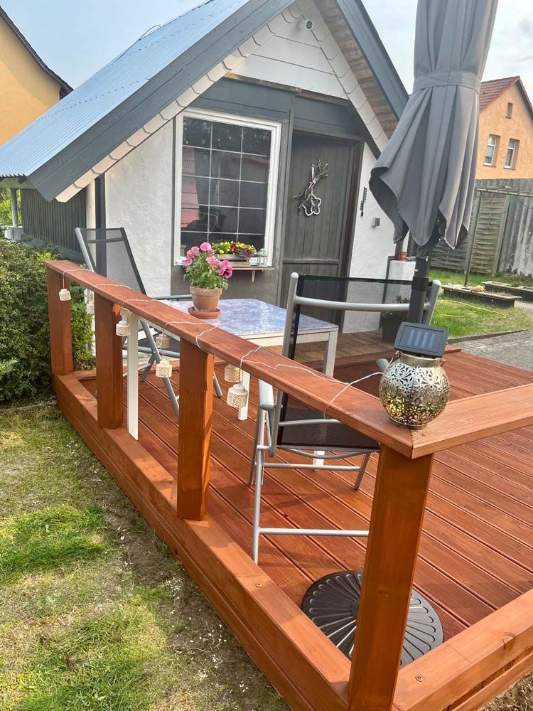 Ein kleines Haus mit einer Holzterrasse und einem Tisch und Stühlen darauf.