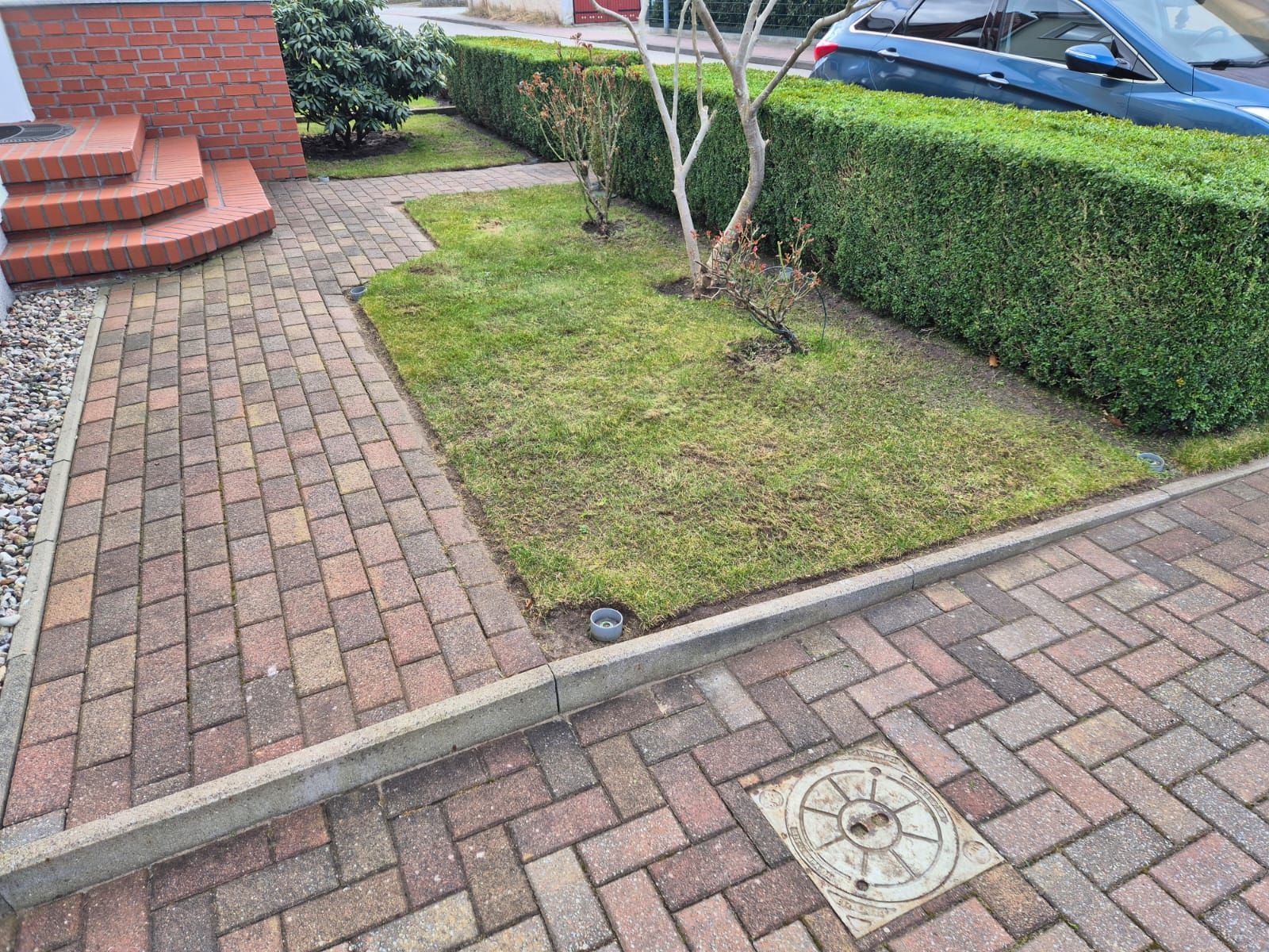 Eine gepflasterte Auffahrt mit einem üppigen grünen Rasen und einem im Hintergrund geparkten Auto.