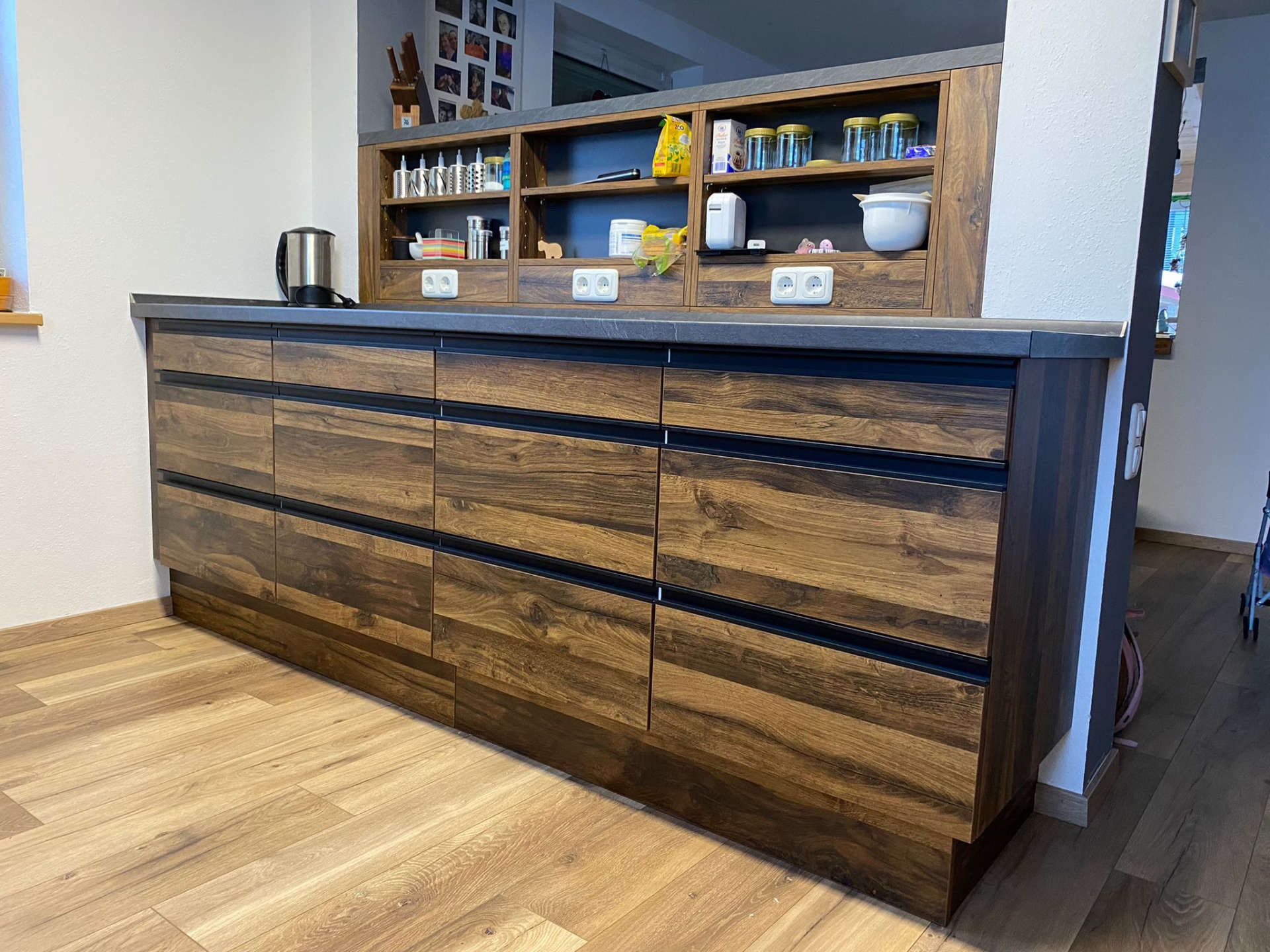 Küchenmodell Fischl Küchentresen aus Holz und integrierte Regale in der Wand darüber von Mihatho von der anderen Seite