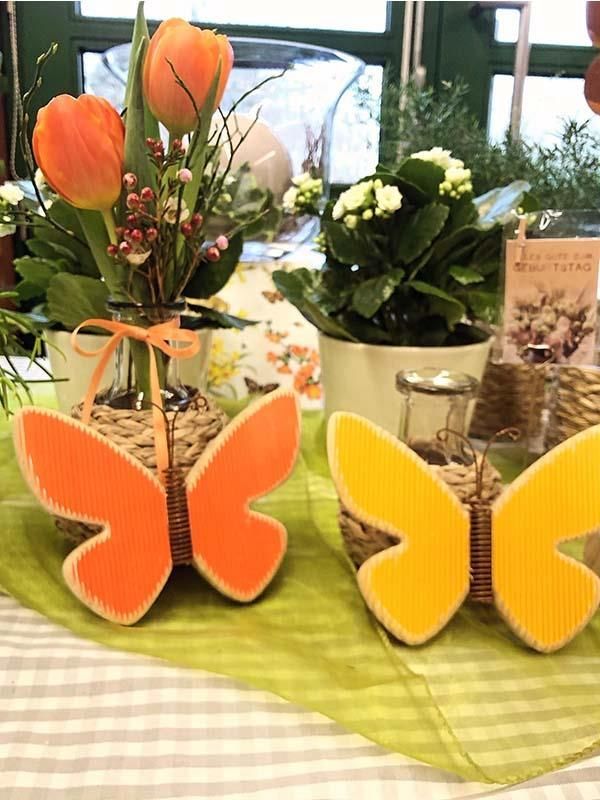 Zwei schmetterlingsförmige Vasen mit Blumen darin auf einem Tisch